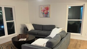Ein Wohnzimmer mit einem grauen Sofa, einem schwarzen Couchtisch und einem gemusterten Teppich.