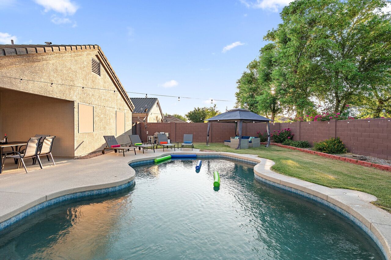 A backyard with a swimming pool, outdoor furniture, and a brick wall.