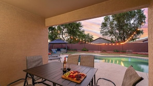 An outdoor patio with a pool, string lights, and a table with a charcuterie board. - Casa Golden Retreat | Heated Pool • Hot Tub • BBQ (Casa Grande)