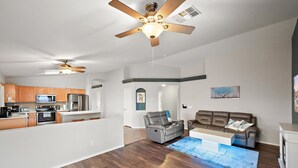 A spacious living area with a gray sofa, a ceiling fan, and a kitchen in the background. - Casa Golden Retreat | Heated Pool • Hot Tub • BBQ (Casa Grande)