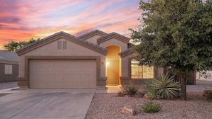 A two-story house with a garage, a covered entryway, and a landscaped front yard with a tree and plants. - Casa Golden Retreat | Heated Pool • Hot Tub • BBQ (Casa Grande)