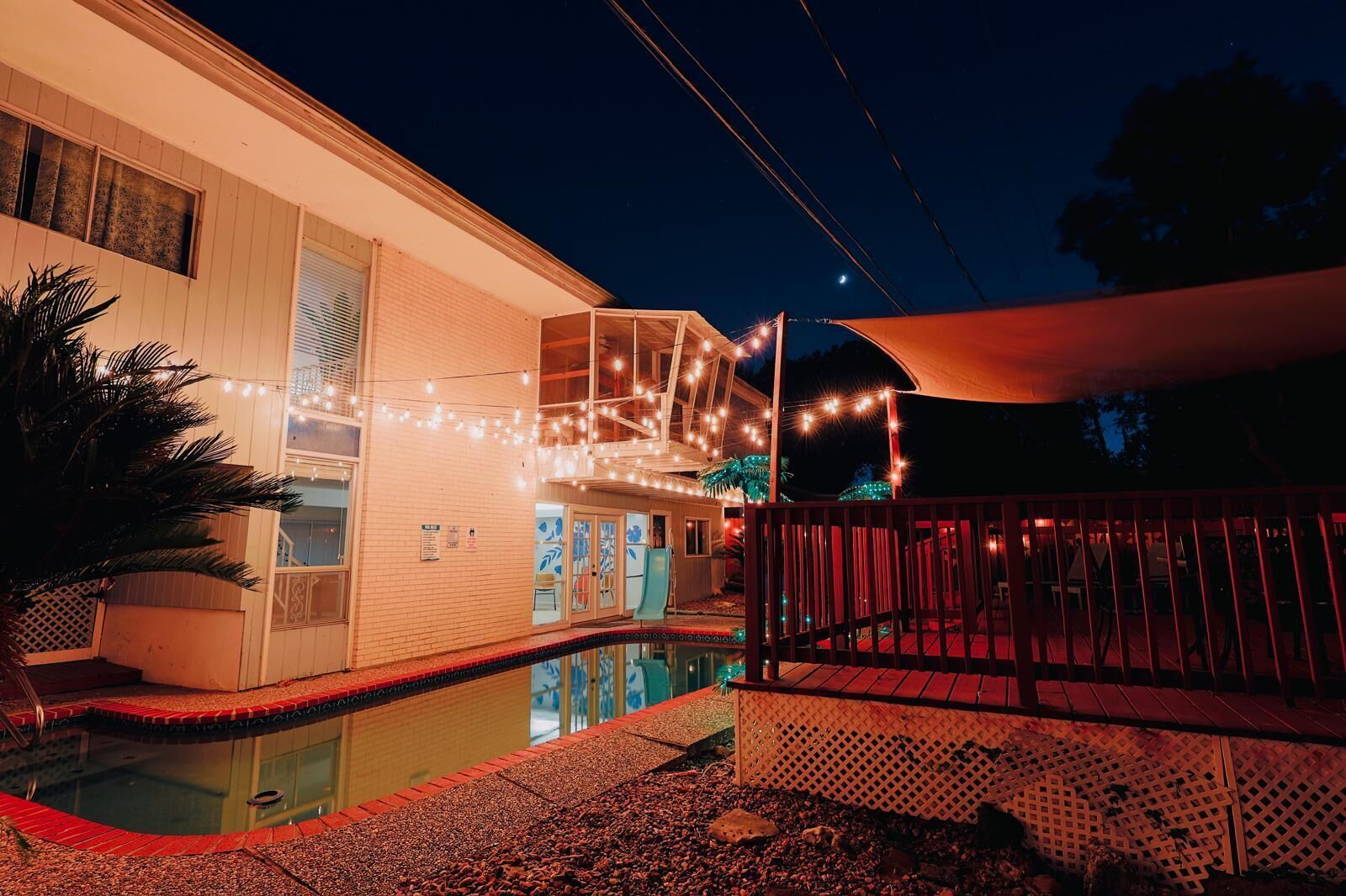 A house with a swimming pool, string lights, and a covered deck area.