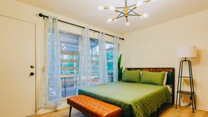 Un dormitorio con cama, banqueta, lámpara y vistas al exterior a través de una ventana.