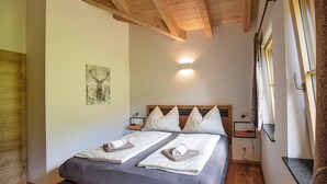 Una cama doble con dos almohadas, cabecero, mesitas de noche, una lámpara de pared e imagen enmarcada en la pared.