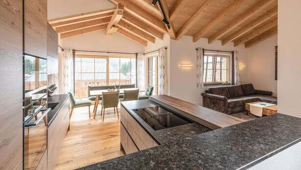 Una cocina moderna con vigas de madera, un comedor con mesa y sillas, y una sala de estar con sofá y mesa de centro.