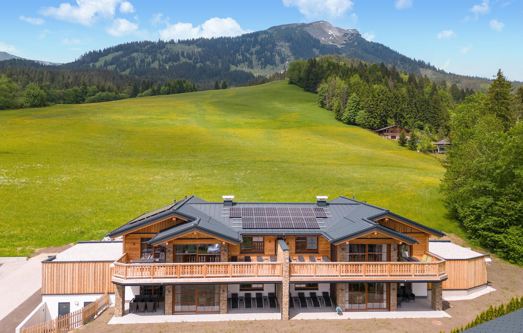 A chalet with a balcony, large windows, and solar panels.