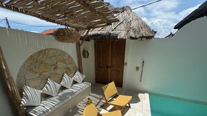 Un espace extérieur ensoleillé, aménagé avec des sièges, un mur en pierre, un toit de chaume et une piscine.