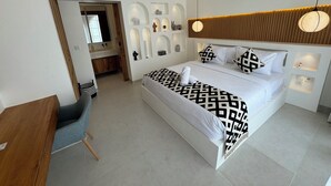 Une chambre d’hôtel moderne avec un grand lit, une tête de lit en bois, une table de chevet et une étagère intégrée agrémentée d’objets décoratifs.