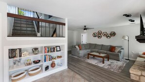 Un salon moderne avec un canapé d’angle gris, une bibliothèque blanche et une table basse en bois.