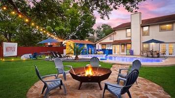 Un jardin avec un foyer, des sièges d’extérieur, une piscine et une maison sur laquelle est apposée une enseigne indiquant « CANTINA ».