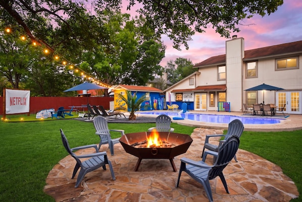Un patio trasero con un brasero, mobiliario exterior, una piscina y una casa con un letrero que dice 'CANTINA'.