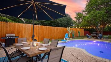 Un espace extérieur aménagé pour les repas, avec une piscine, une clôture en bois et du mobilier de jardin.