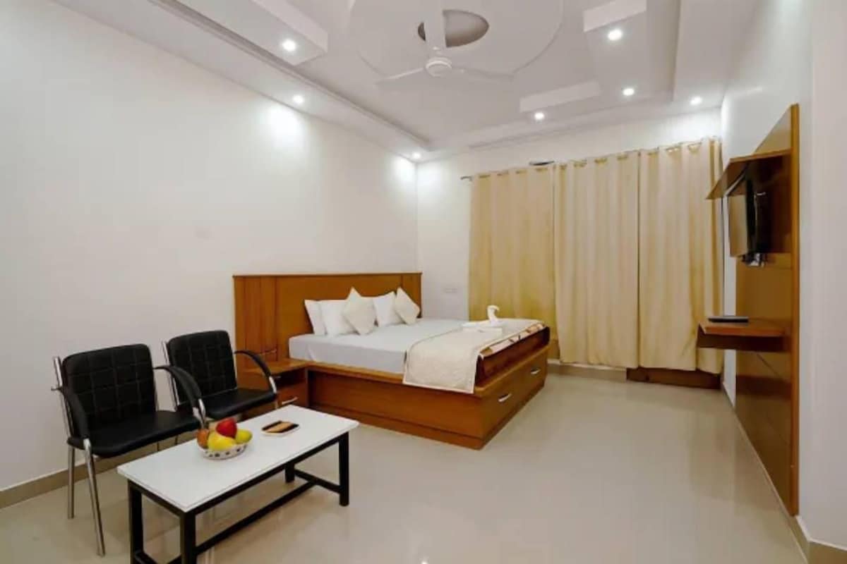 A modern bedroom with a bed, two black chairs, a small table with fruit, and a TV on a stand.