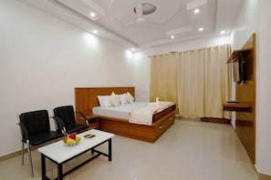 A modern bedroom with a bed, two black chairs, a small table with fruit, and a TV on a stand. - Hotel Roop Mandi (Manali)