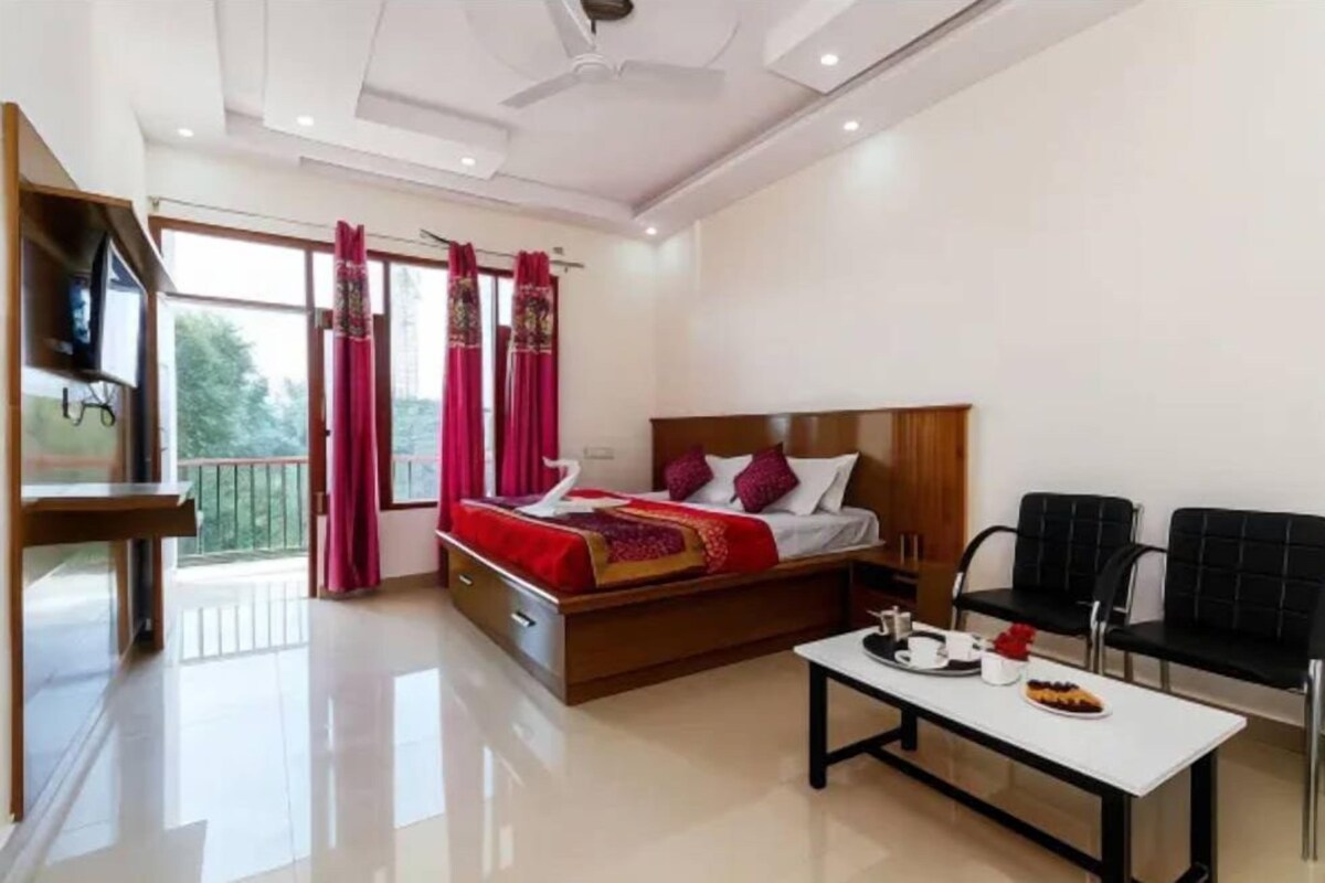 A hotel room with a bed, a small table with a plate of food, a TV, and a balcony with red curtains.
