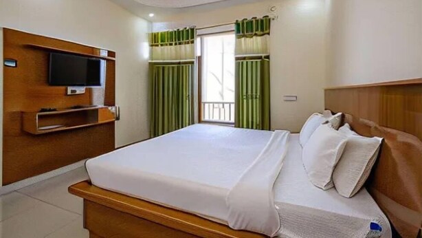 Una habitación de hotel con una cama, un televisor en la pared y una ventana con cortinas.