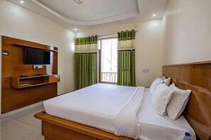 A hotel room with a bed, a television mounted on the wall, and a window with curtains. - Hotel Roop Mandi (Manali)