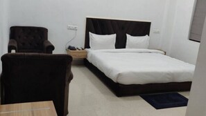Quarto de hotel com uma cama de solteiro, uma cadeira, uma mesa de cabeceira e um criado-mudo.