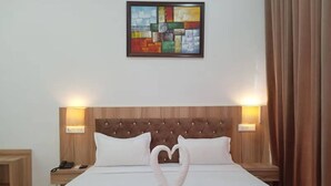 Ein Hotelzimmer mit einem großen Bett, zwei Nachttischlampen, einem Wandbild und einer dekorativen Schwanen-Handtuch-Arrangement.