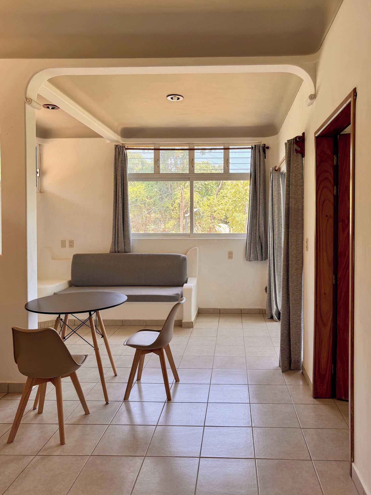 A room with a dining table, chairs, a sofa, and a window with curtains.