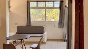 A room with a dining table, chairs, a sofa, and a window with curtains.