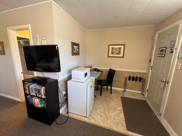 Une chambre d’hôtel compacte équipée d’un téléviseur à écran plat, d’un petit réfrigérateur, d’une bibliothèque, d’un bureau et d’une chaise.