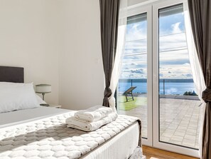 Un dormitorio con cama, mesita de noche, lámpara y vistas a un balcón con silla y mesa.