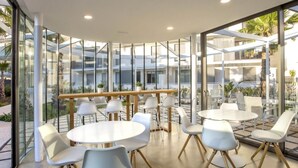 Uma sala de jantar moderna e interna, com paredes de vidro, mesas redondas brancas e cadeiras contemporâneas.