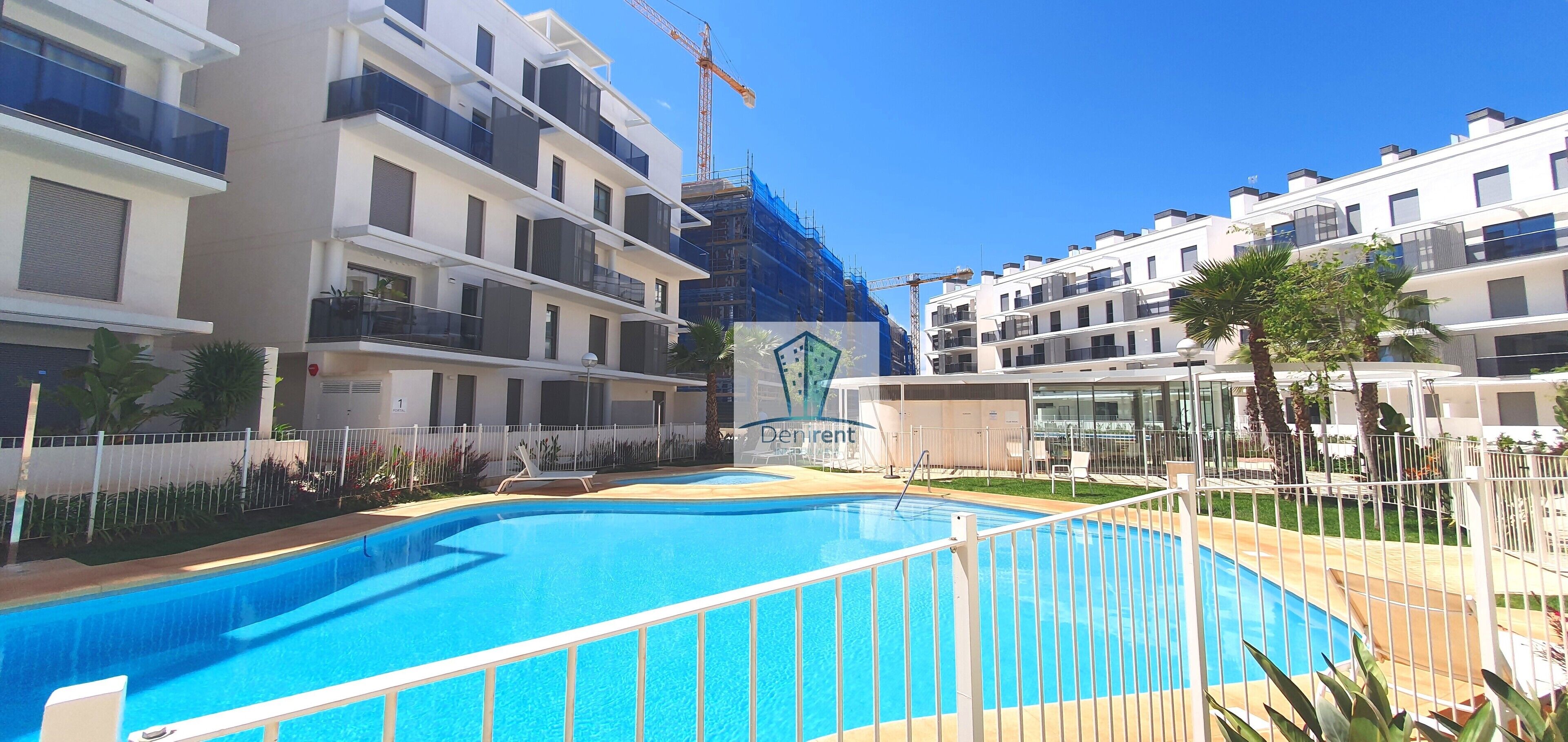 Un immeuble d’appartements moderne doté d’une piscine, de balcons, et avec des grues de construction visibles en arrière-plan.