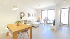 Sala de estar moderna com mesa de jantar de madeira, sofás brancos e uma grande porta de vidro deslizante que dá para um pátio externo.