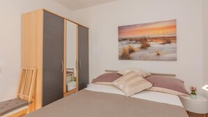 A bedroom with a bed, a wardrobe, a chair, a bedside table with a plant, and a painting of a sunset. - Lovely apartment in Vir with WiFi (Vir)