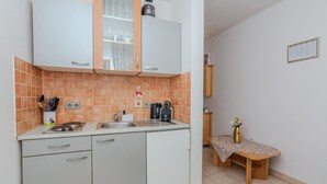 A compact kitchen with white cabinets, a sink, and a coffee maker. There's a small table with a vase of flowers and a wooden bench. - Lovely apartment in Vir with WiFi (Vir)