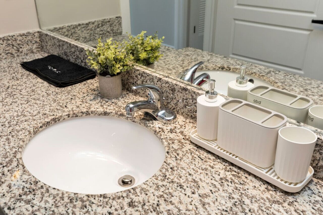 Un lavabo de salle de bain avec un plan de toilette en granit, une petite plante en pot, une serviette noire et un ensemble de produits de toilette blancs.