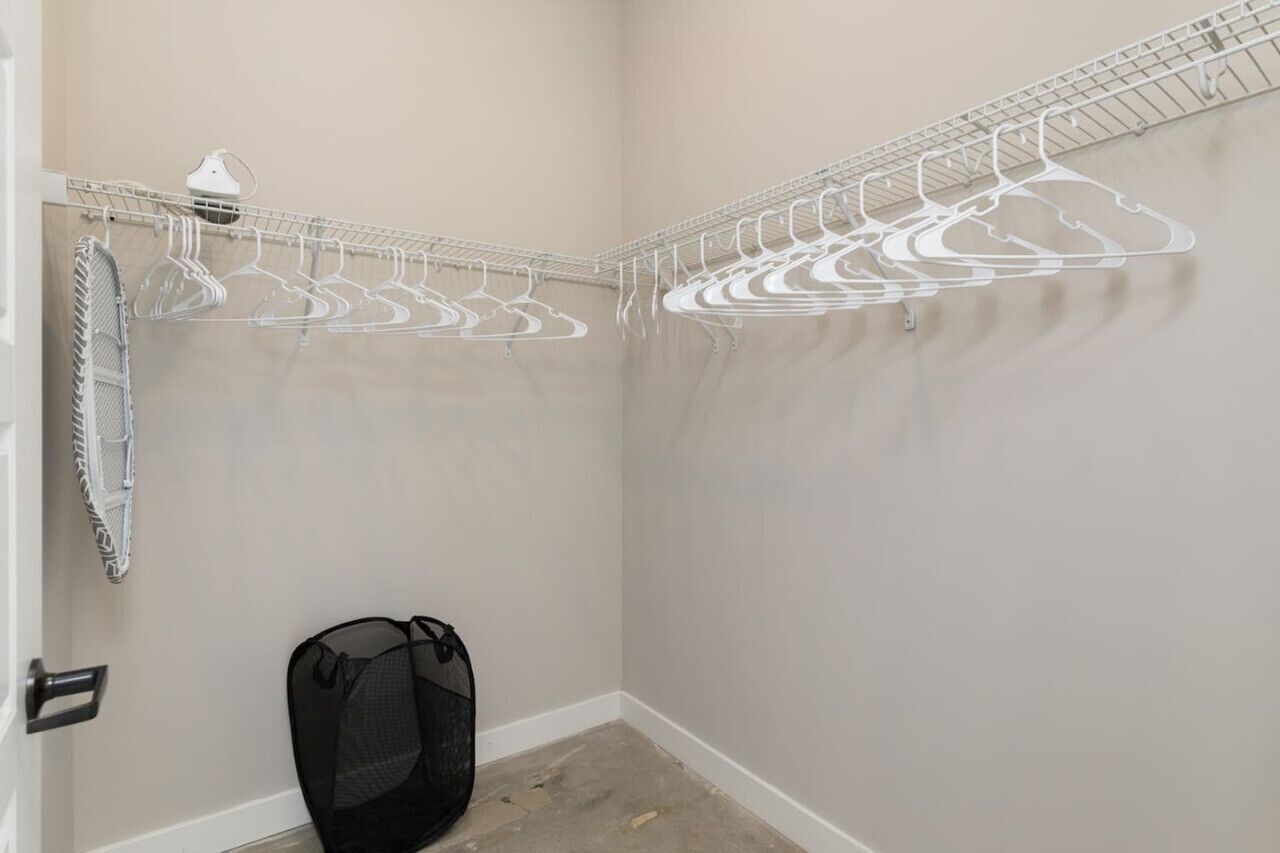 A corner closet with a wire shelving unit holding multiple hangers, a black mesh laundry basket, and a white towel rack.