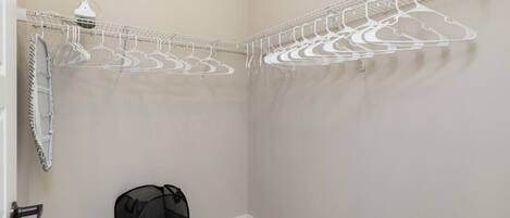 A corner closet with a wire shelving unit holding multiple hangers, a black mesh laundry basket, and a white towel rack.