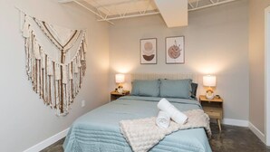 Un dormitorio con una cama, dos mesitas de noche, un tapiz en la pared y dos cuadros enmarcados.