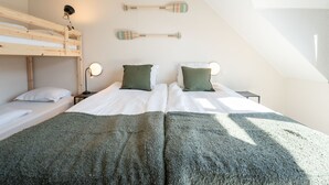 Et værelse med køjesenge, to sengeborde med lamper og et surfbræt hængt på væggen.