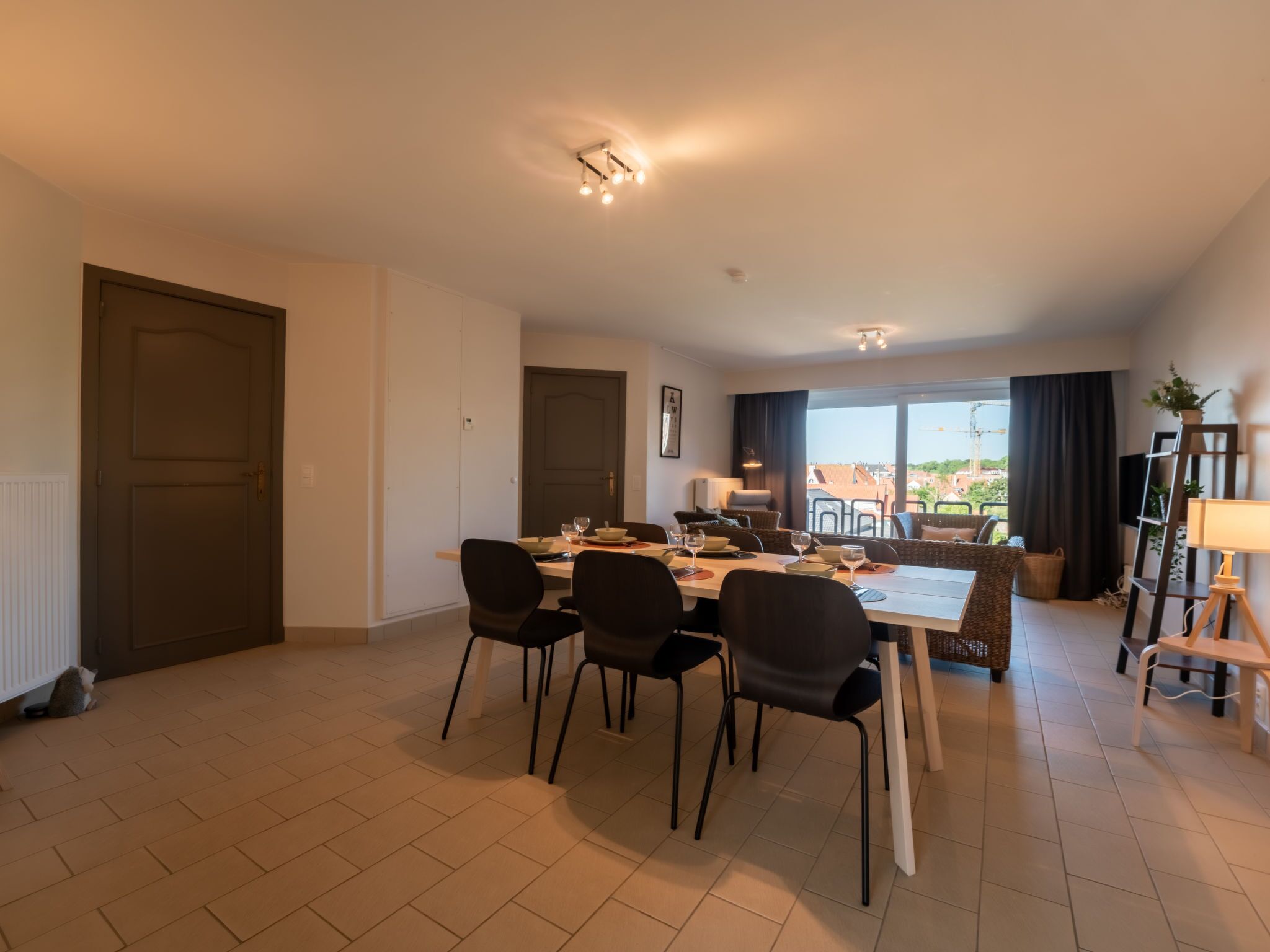 Un espace de restauration moderne, avec une table dressée pour quatre personnes, entourée de chaises, et offrant une vue sur la ville grâce à de grandes fenêtres.