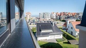 Zona residenziale con vista su un parcheggio, un piccolo edificio con tetto spiovente e una fila di case con tetti in tegole rosse.