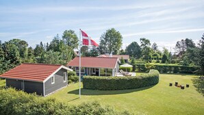 Ein Wohngebiet mit einem Haus, das ein rotes Ziegeldach, eine überdachte Terrasse und eine Fahnenstange mit einer Flagge hat.