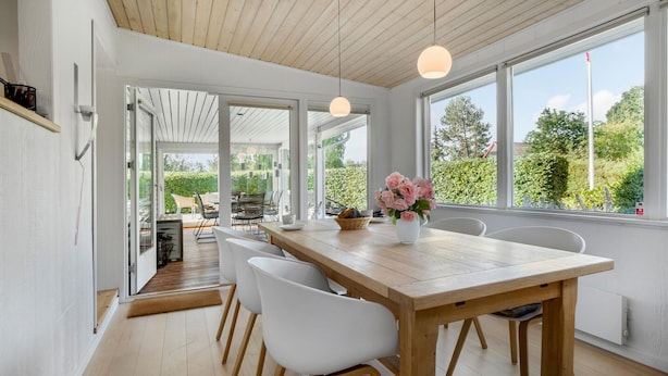 Ein zeitgemäßer Essbereich mit einem Holztisch, weißen Stühlen und Blick auf den Garten durch große Fenster.