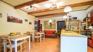 Una cuina acollidora amb bigues de fusta, una zona de menjador amb taula i cadires, i un espai de saló amb sofà.