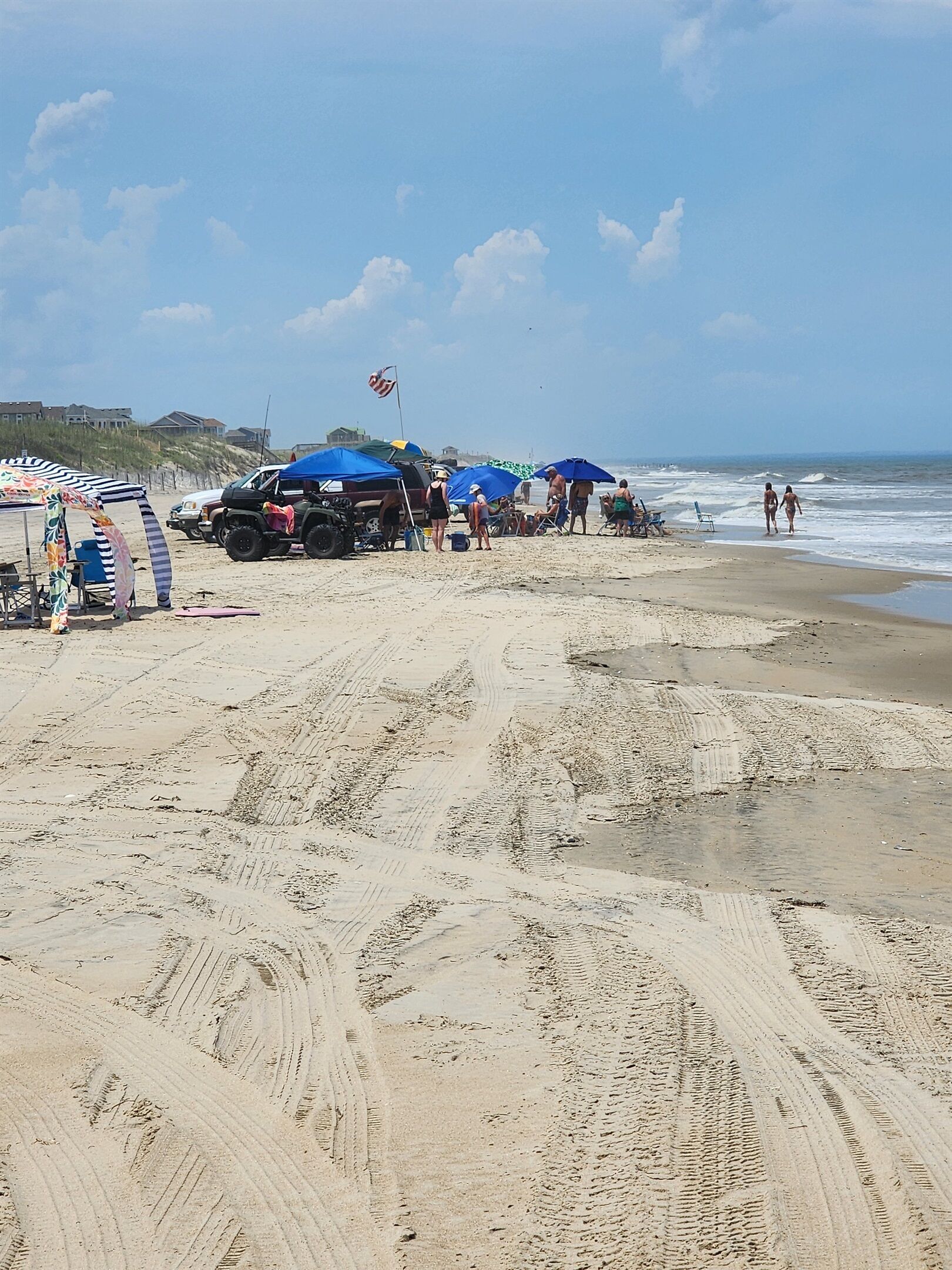 Ein Sandstrand mit Fußabdrücken, Zelten und einem Fahrzeug.
