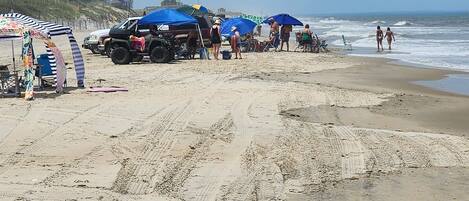 Ein Sandstrand mit Fußabdrücken, Zelten und einem Fahrzeug.