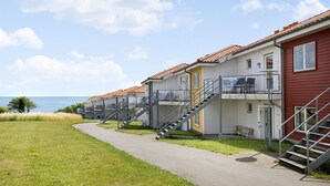 A row of seaside cottages with external staircases leading to balconies, a paved walkway, and a clear view of the sea.