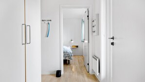 A narrow hallway with a bed in the distance, a radiator, and a coat rack with a blue item hanging.