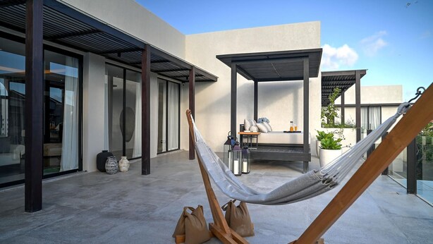 Una hamaca en un espacio exterior moderno con puerta de cristal, una zona de estar techada y vista al cielo.