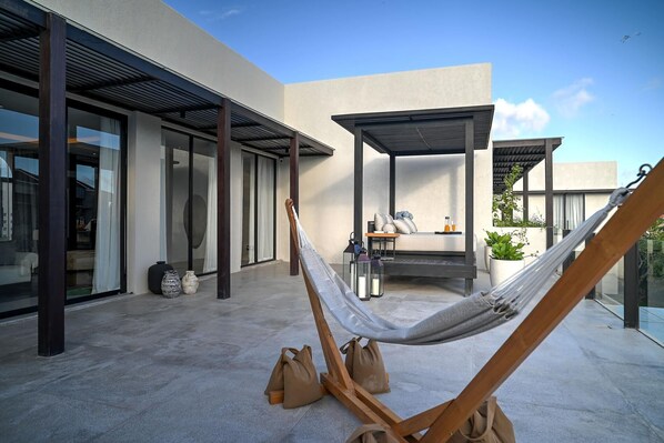 Un hamac dans un espace extérieur moderne, avec une porte vitrée, un coin salon abrité et une vue sur le ciel.