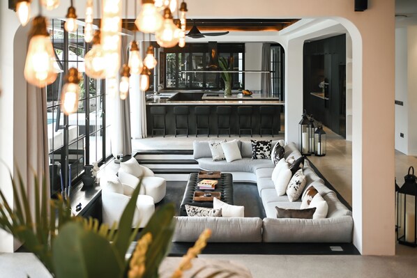 Un salon moderne avec un grand canapé, une table basse et un coin cuisine à l’arrière-plan.