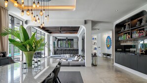 A modern kitchen with a large island, a dining area with chairs, and a bar area with shelves of bottles and glasses. - CARPEDIEM VILLA BALI operated by Villa Nila (Canggu)